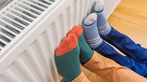Two pairs of feet wearing socks warming themselves against a heater